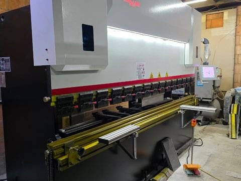 Plegadora CNC vista en escorzo desde el extremo izquierdo dentro de un taller: pórtico en C blanco con el logo INGELASER.
