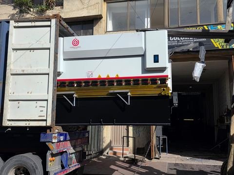 Plegadora CNC saliendo del contenedor sobre la mula, suspendida a la altura del portón del taller durante la descarga.