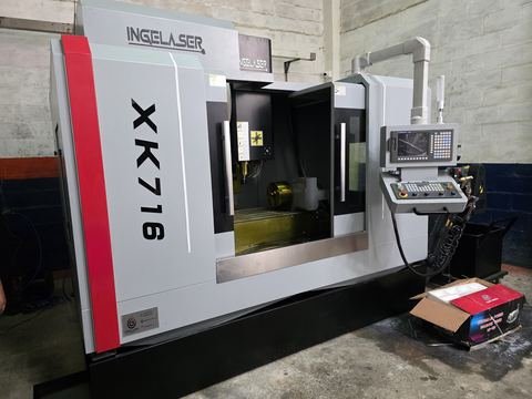 Fresadora CNC de columna rotulada XK716 en nave de taller, vista 3/4 desde la izquierda con la puerta corrediza abierta.