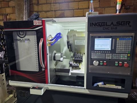 Torno CNC tipo gang con la puerta corrediza abierta en un taller de pared de ladrillo: se ve el plato.