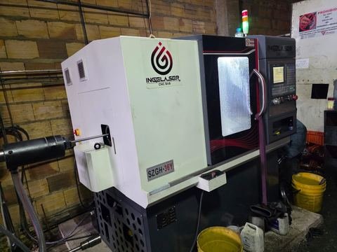 El mismo torno CNC compacto en tres cuartos desde el lado del cabezal, con la barra de material entrando por el husillo.