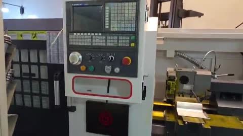 Torno CNC de taller: consola con control CNC de teclas, plato de tres mordazas naranja.
