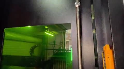 Corte visto a través del vidrio verde de protección de una máquina de cabina cerrada: el haz y las chispas trabajan.