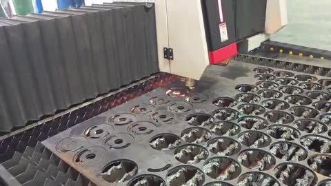 Corte láser de lámina en producción: el cabezal recorre un nido de discos y anillos ya cortados sobre los listones.