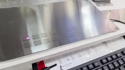 Marcadora láser de sobremesa grabando: primero el detalle de una placa de acero inoxidable con texto marcado en filas.