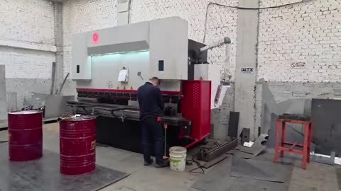 Un operario dobla lámina en una plegadora CNC de pórtico en C dentro de una nave de ladrillo pintado: se le ve posicionando.